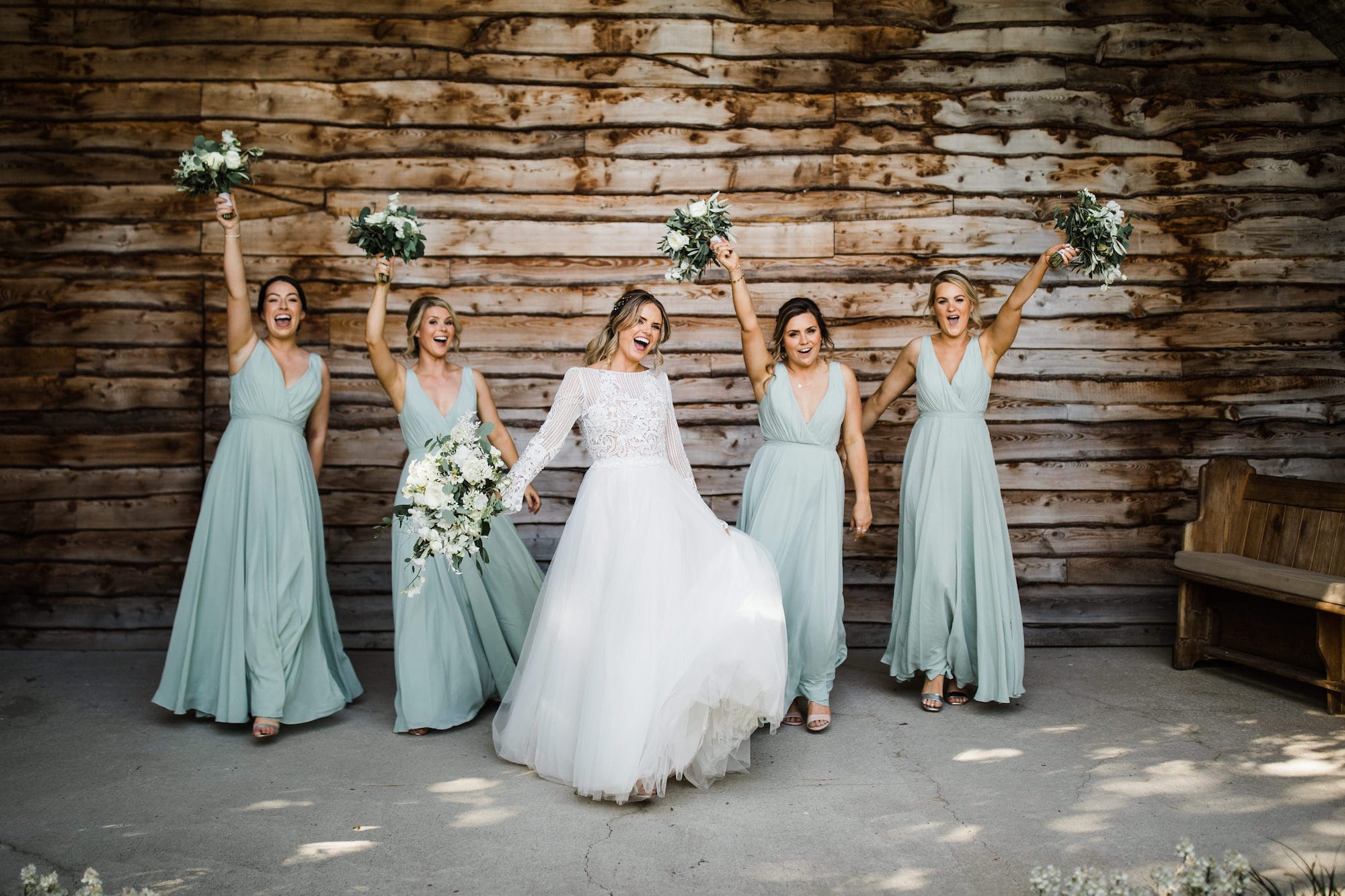 spring bride celebrates with her bridal party beneath the sandstone arh of the Old Railway Bridge - outdoor ceremony area at Tower Hill Barns.