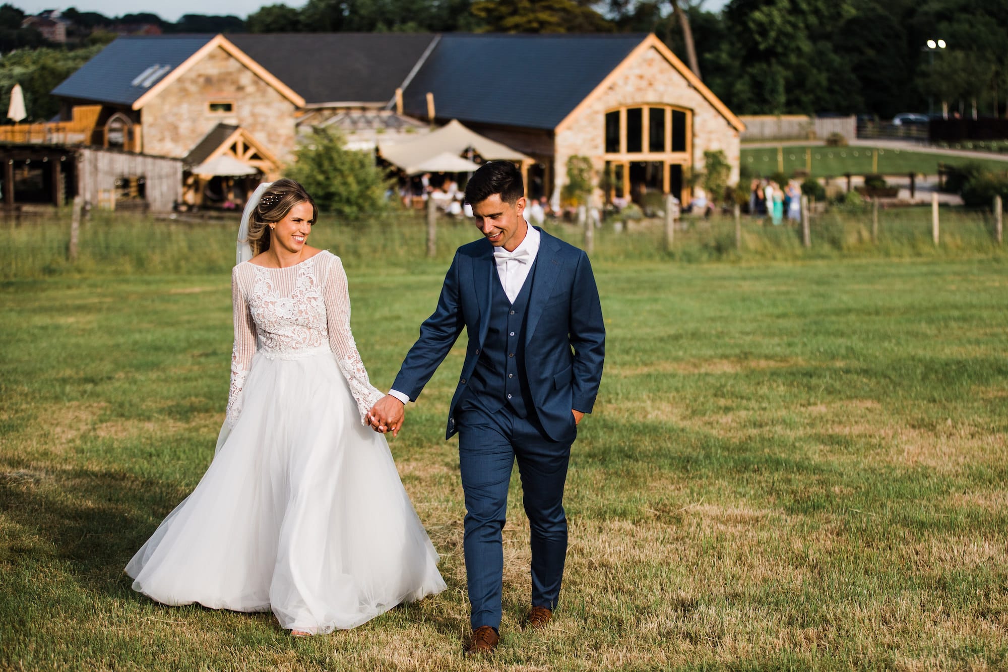 Newlywed couple stroll through a field overlooking Tower Hill Barns countryside wedding venue.