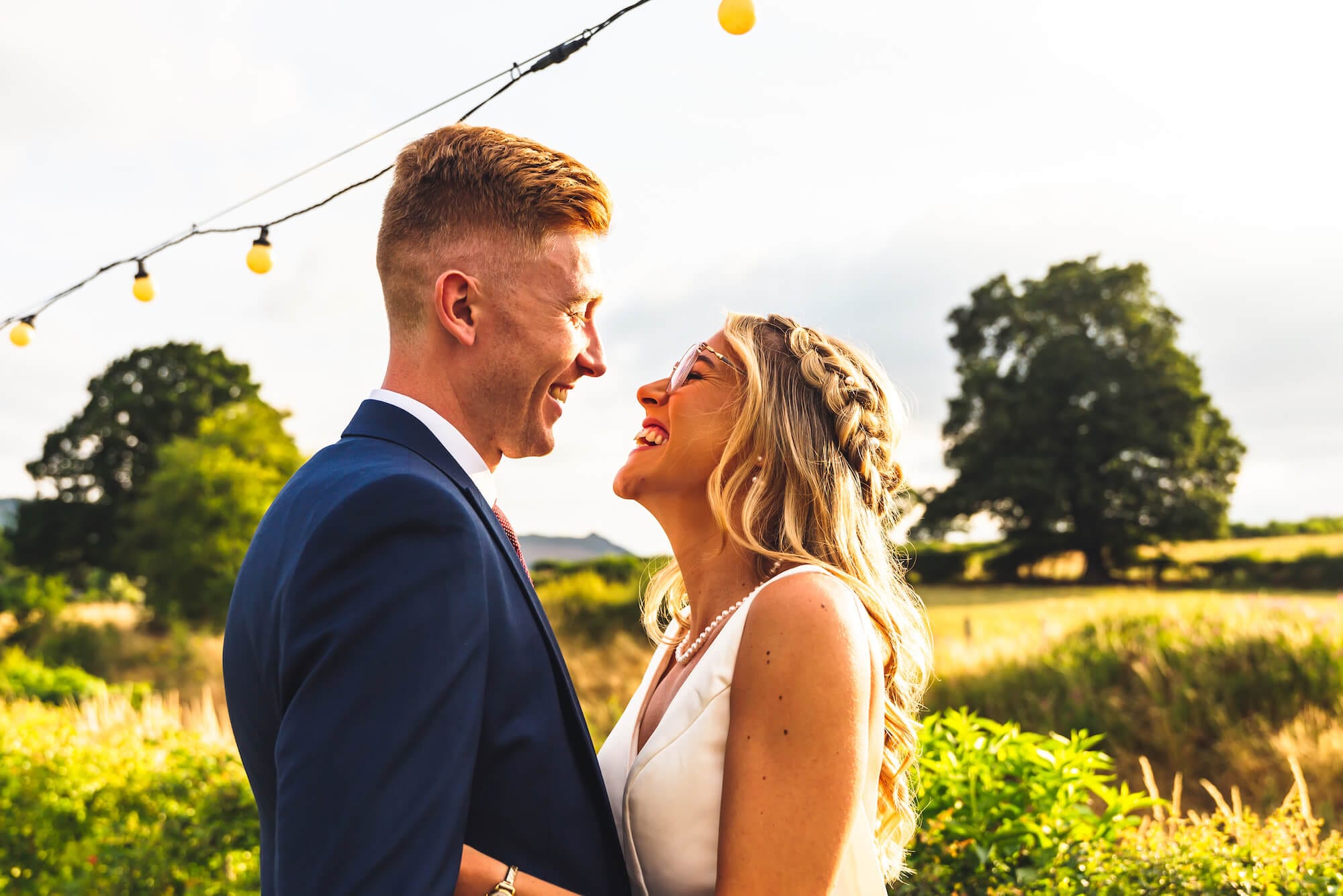 Newlyweds Alison and Jack embrace following their outdoor wedding ceremony at Tower Hill Barns. In the background rolling views over the North Wales countryside.