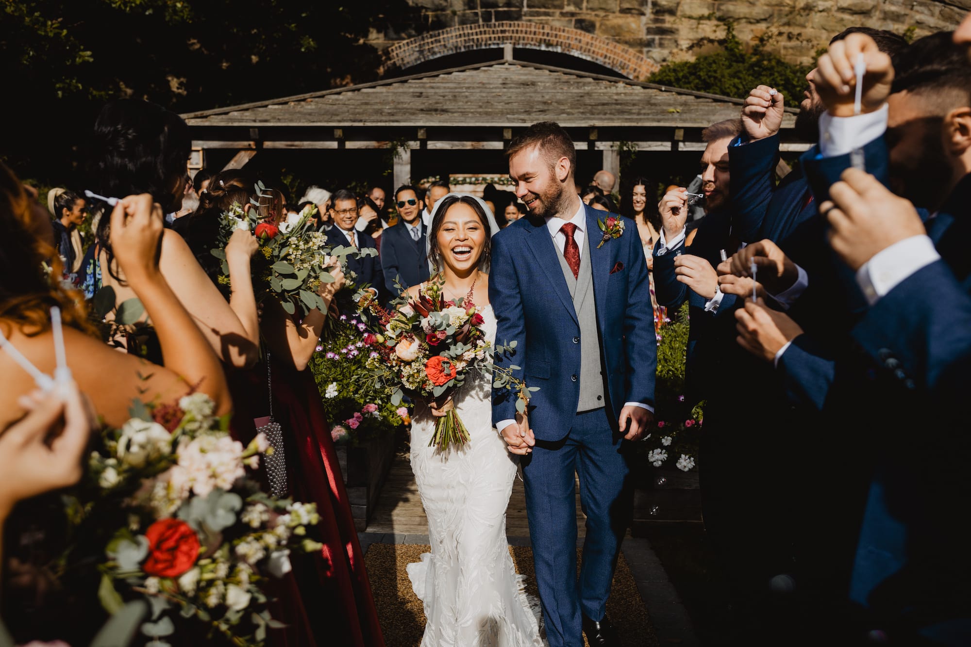 Couple bound happily out of the outdoor ceremony area at Tower Hill Barns as their guests blow bubbles following their civil ceremony at Tower Hill Barns facilitated by a Wrexham Registrar.