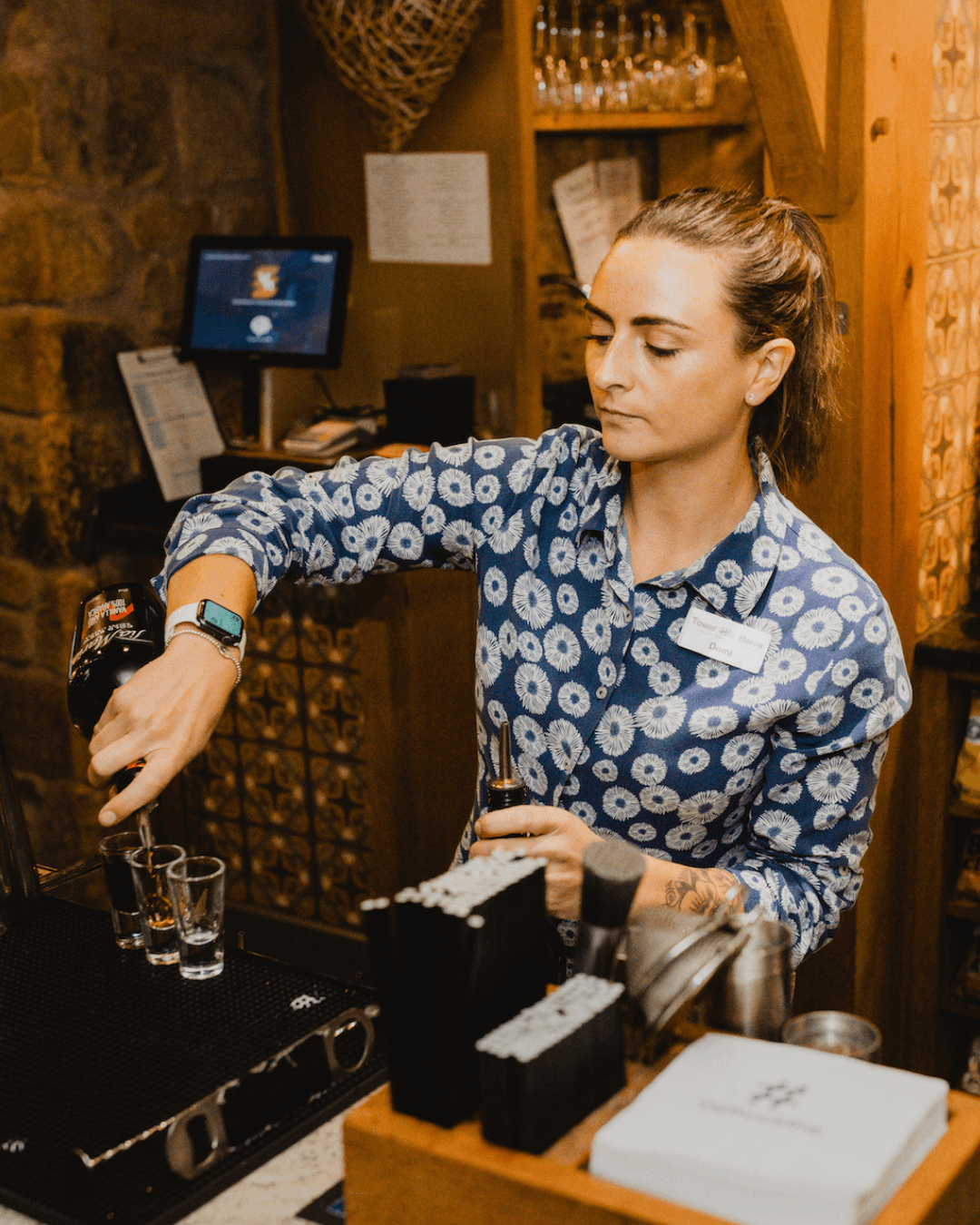 Domi pours a drink into a shot glass on the bar at Tower Hill Barns.