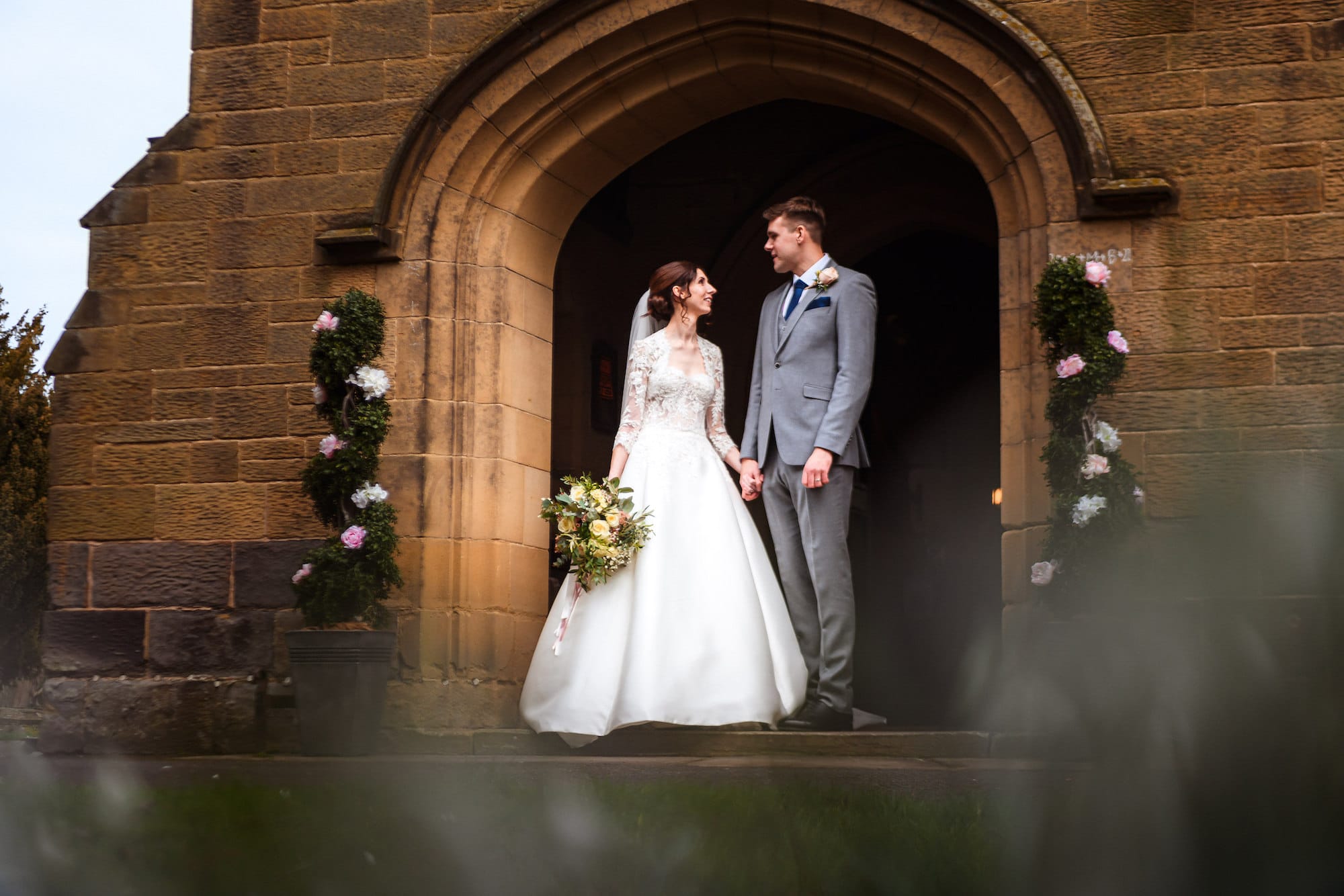 Newlyweds Emily & Ben stand outside the church following their traditional church ceremony.