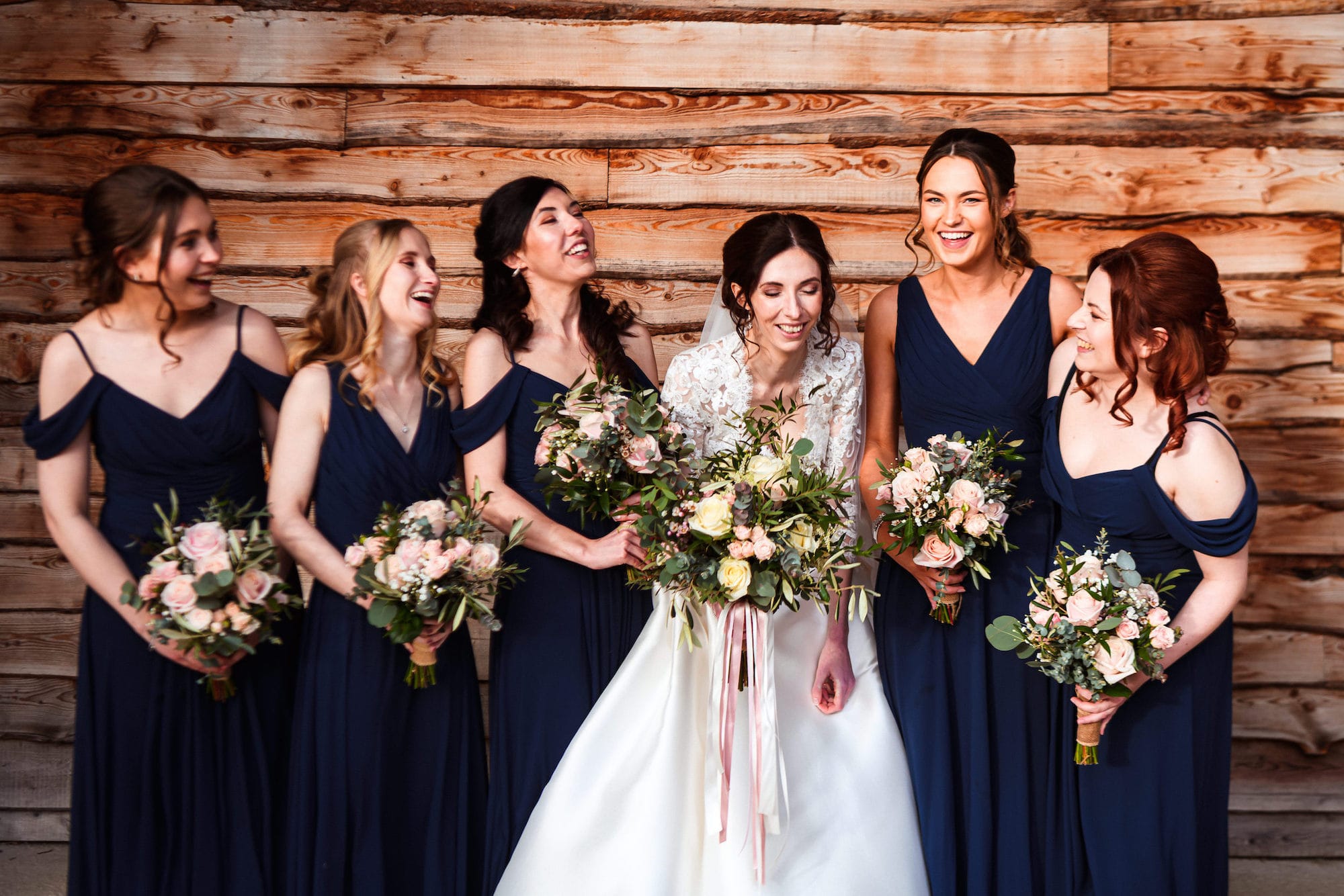 Bride and her bridal party laugh together beneath the Old Railway Bridge at Tower Hill Barns.