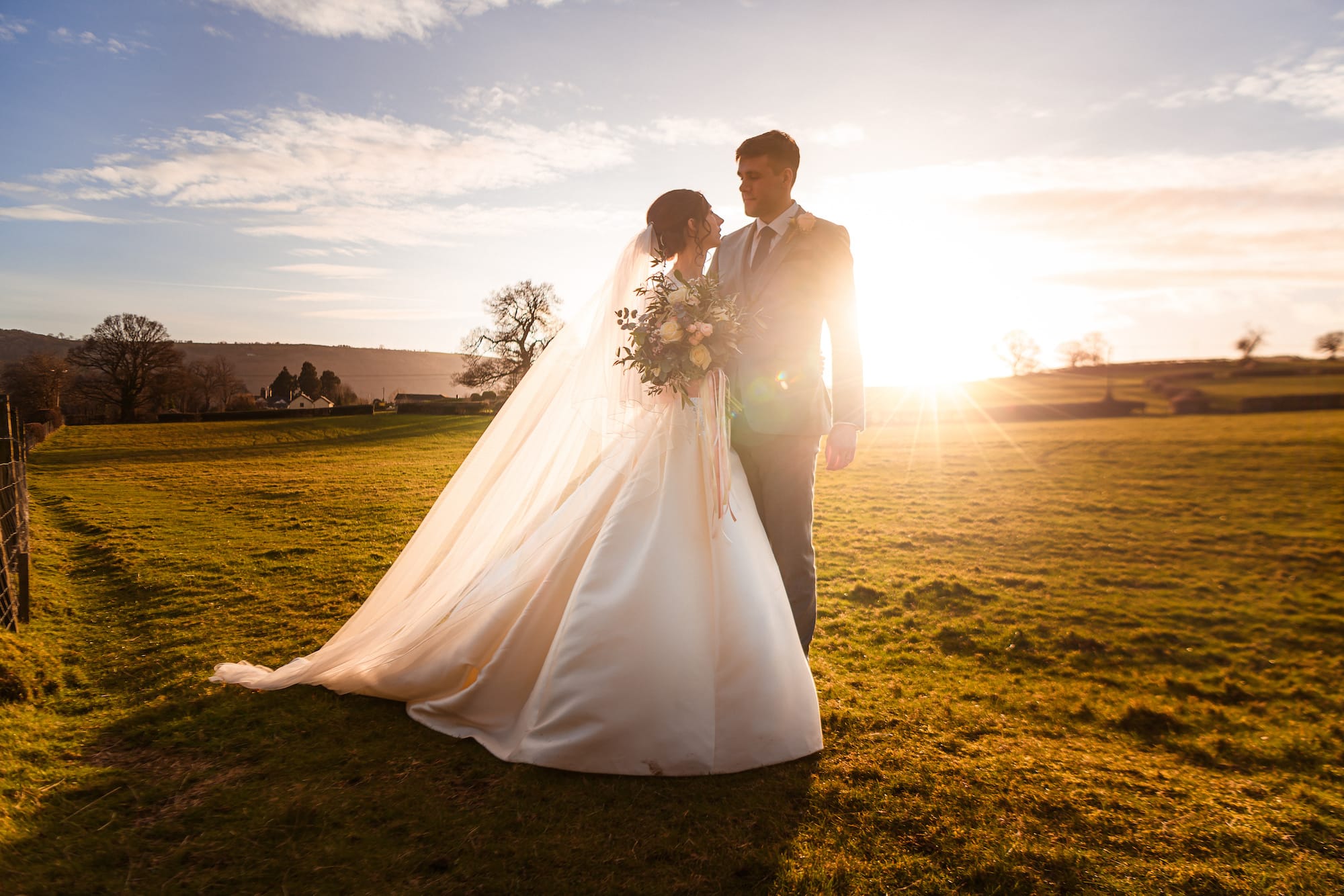 A bride and groom stroll through the rolling Welsh countryside surrounding their wedding reception venue - Tower Hill Barns following their winter church wedding.