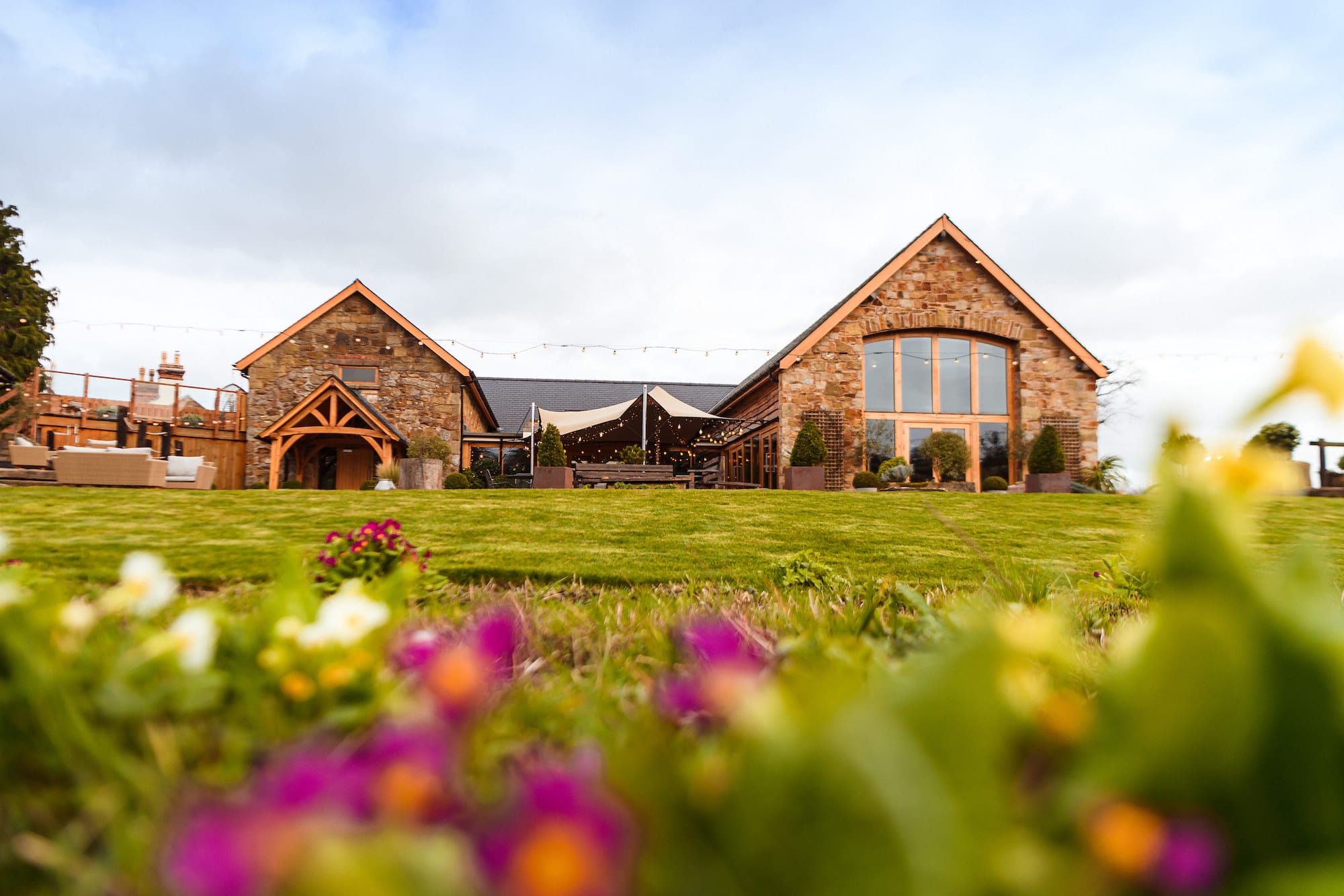 Tower hill Barns Venue Shot in the foreground flowers and a manicured lawn lead to the wedding venue.